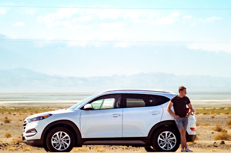 man standing next to car in desert